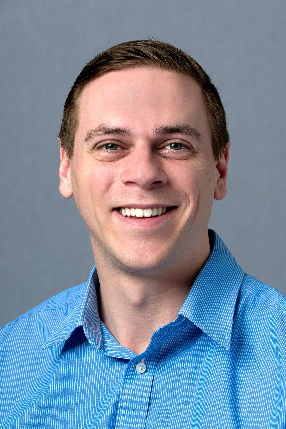 Austin Adair, owner of Affordable Home Care, smiles warmly in a blue pinstripe dress shirt.